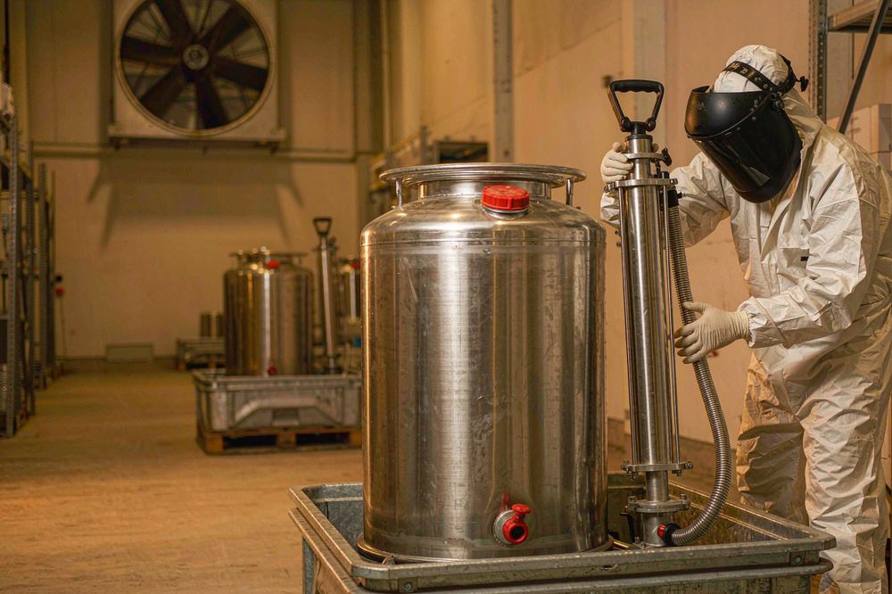 Worker in protective suit connecting a drum pump to a DETA steel drum