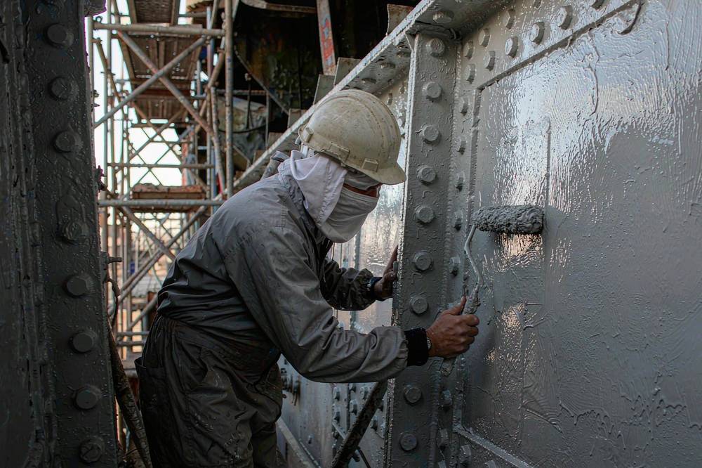 Marine epoxy coating applied by roller to a steel hull section in a shipyard